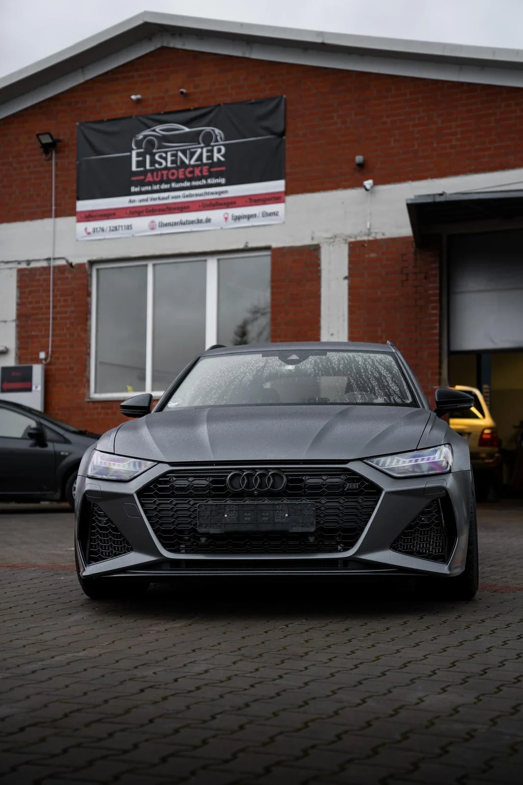 Halle der Elsenzer Autoecke in der Elsenzstraße mit Firmenschild, davor ein dunkelgrauer Audi Kombi