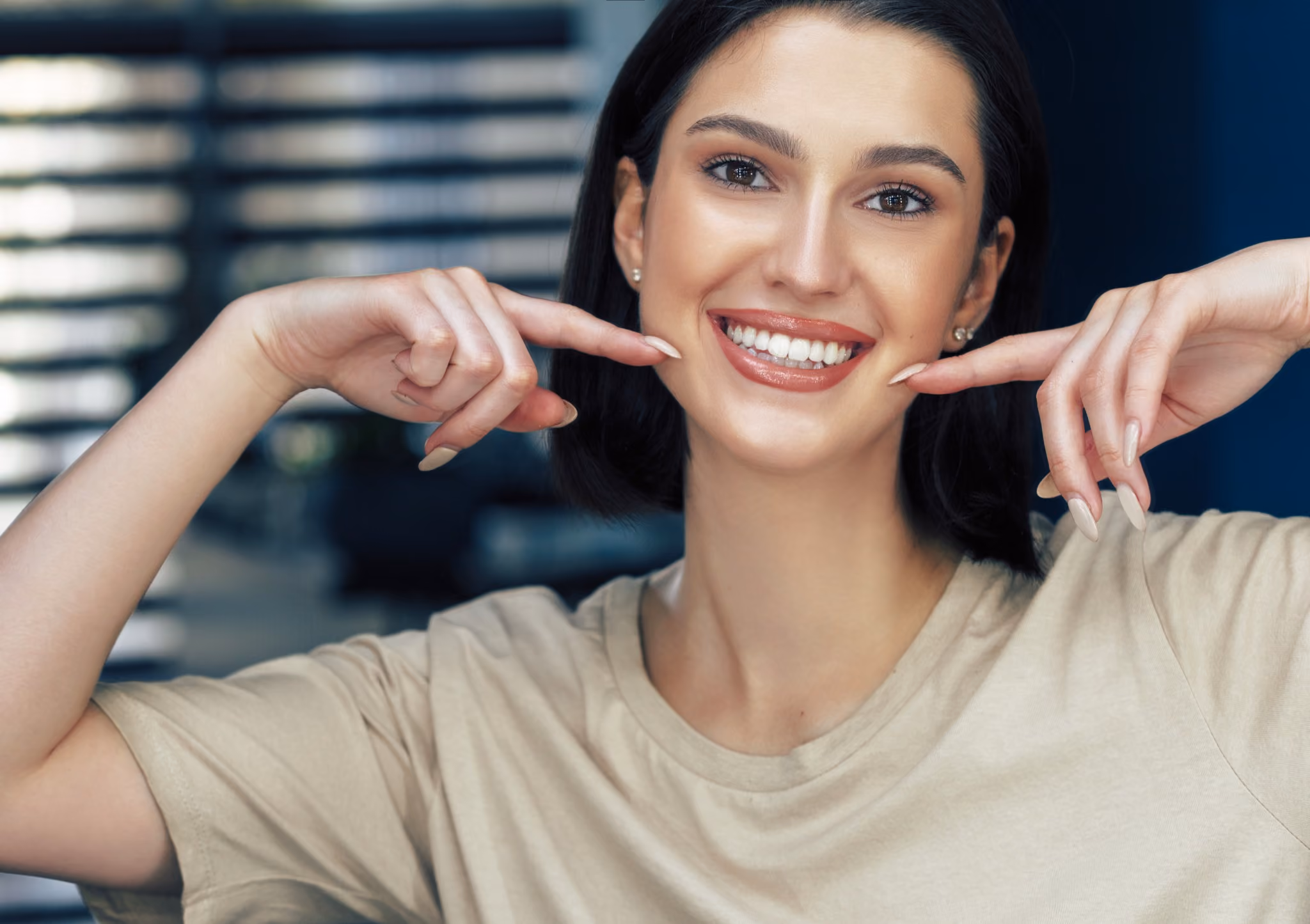Smiling woman pointing toward her teeth with both index fingers to highlight her healthy smile.