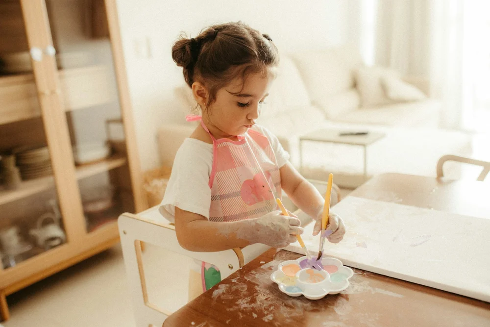 A young girl painting at a small table in a bright room
