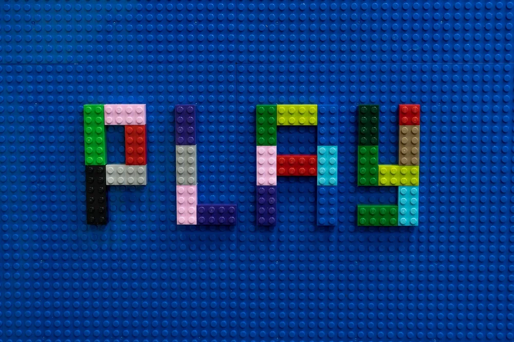 The word PLAY spelled out in building bricks on a blue baseplate