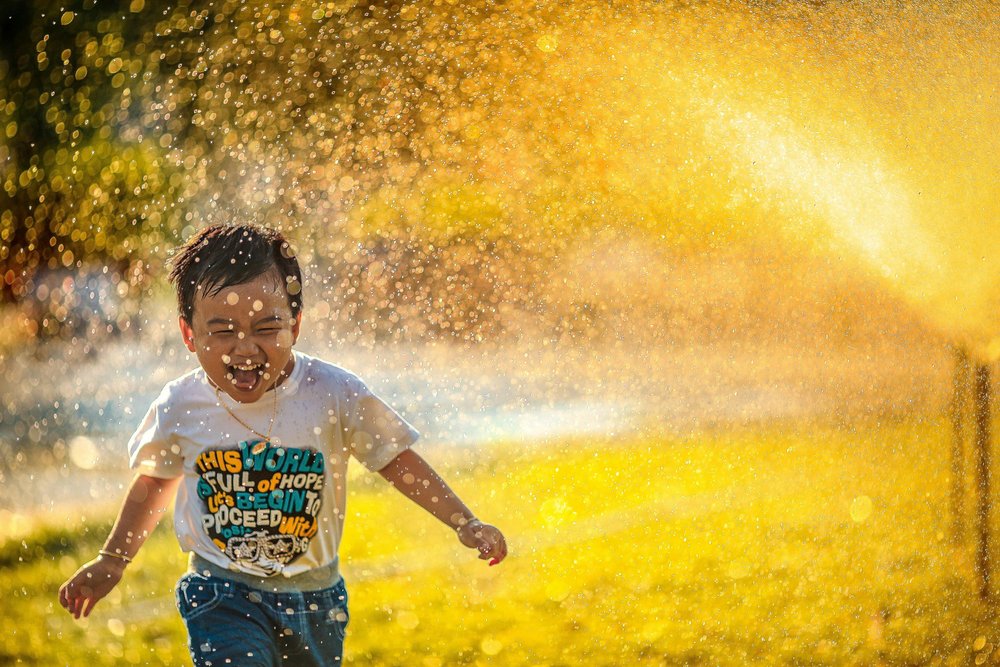 A child running through a garden sprinkler in the sunshine