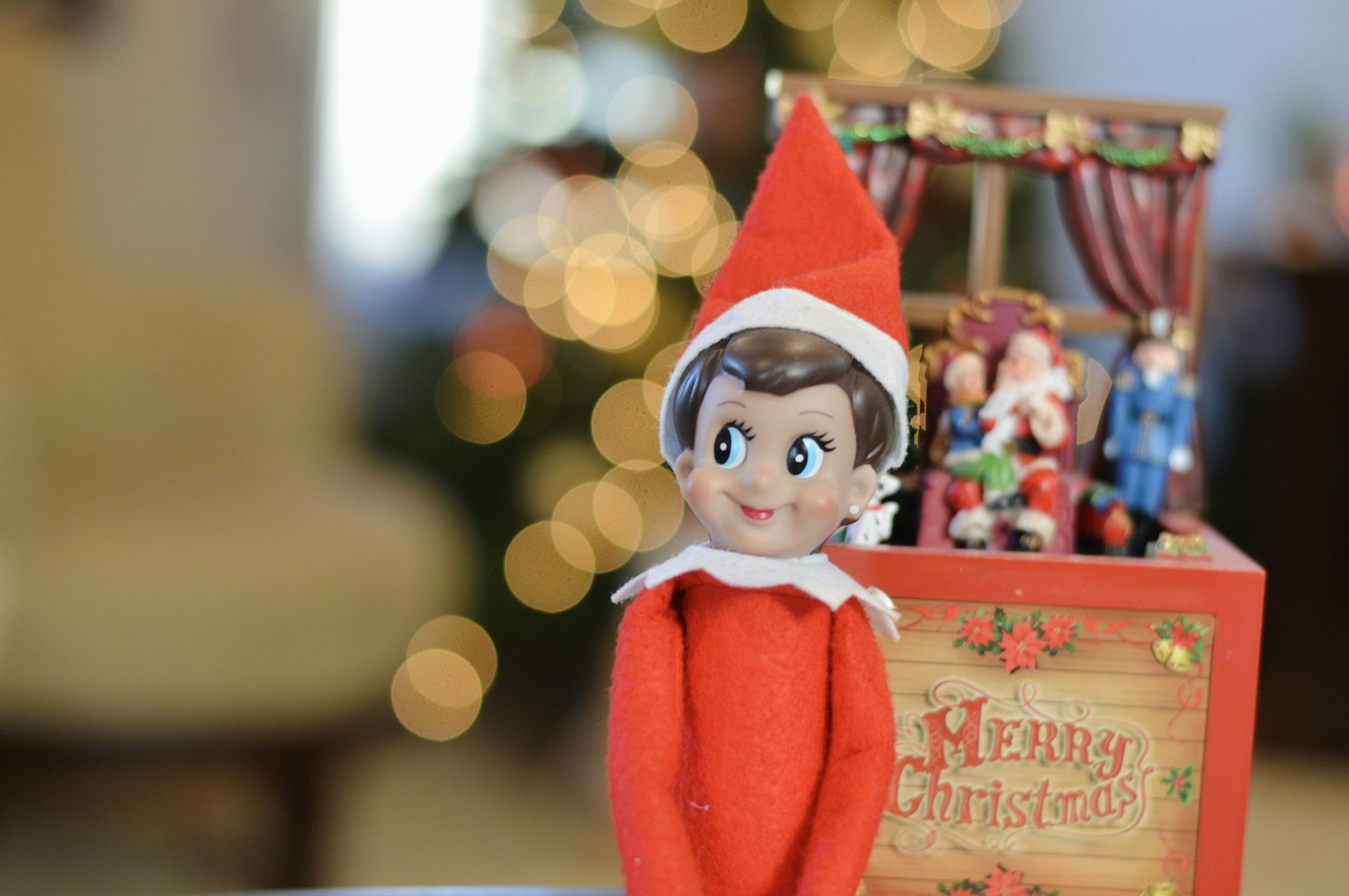 An Elf on the Shelf doll propped beside a Christmas display