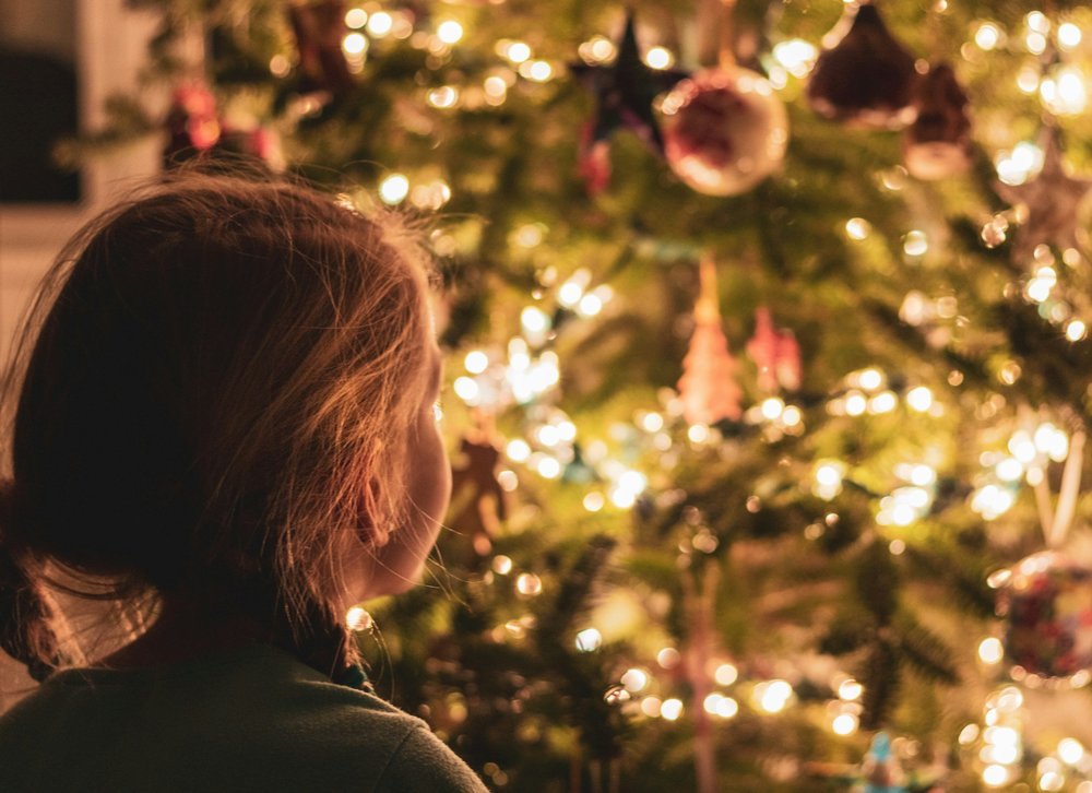 A child looking up at a lit Christmas tree