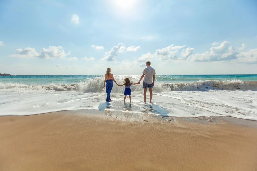A family of three standing at the edge of the surf, seen from behind