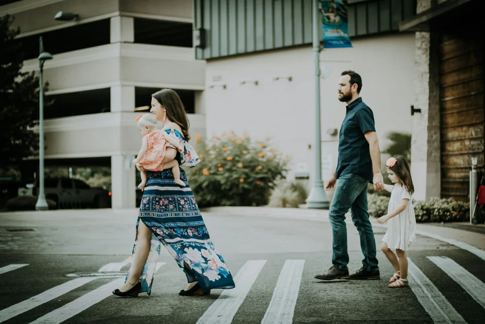 A family crossing a street, one parent walking ahead of the other and a child