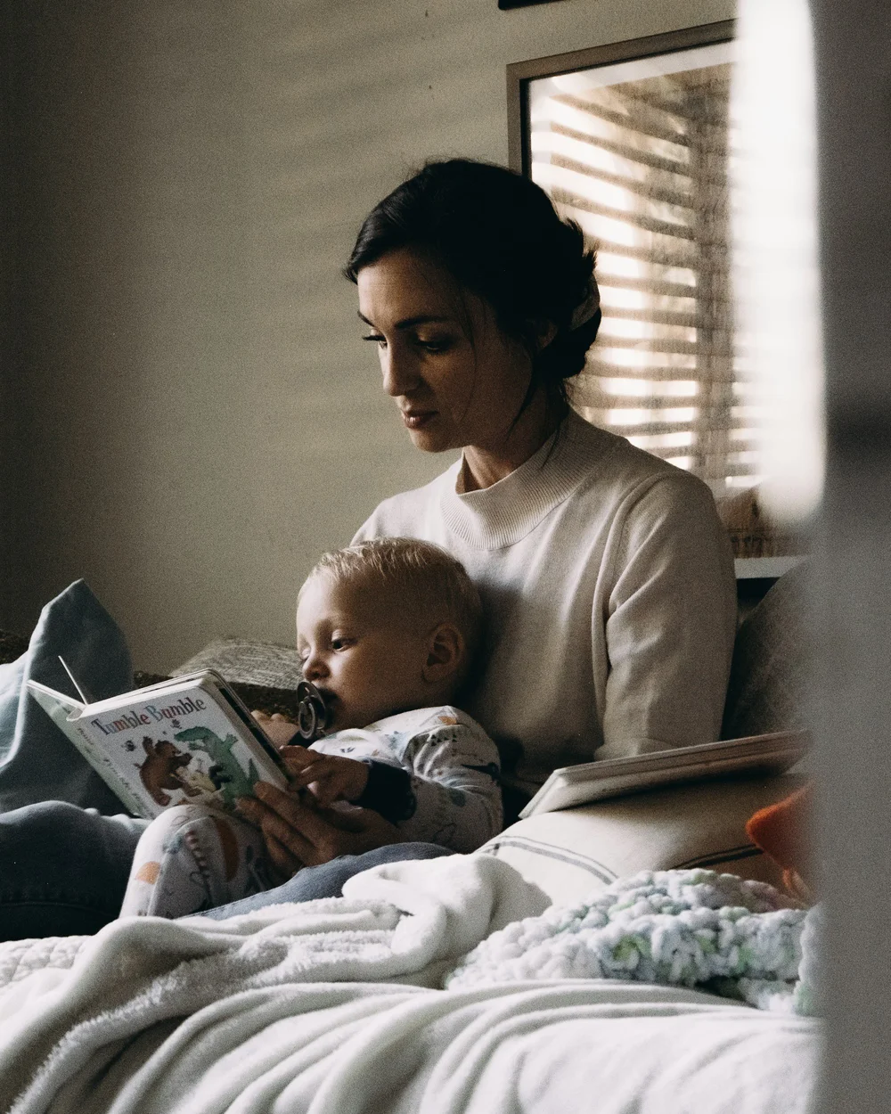 An adult reading a picture book in bed with a young child