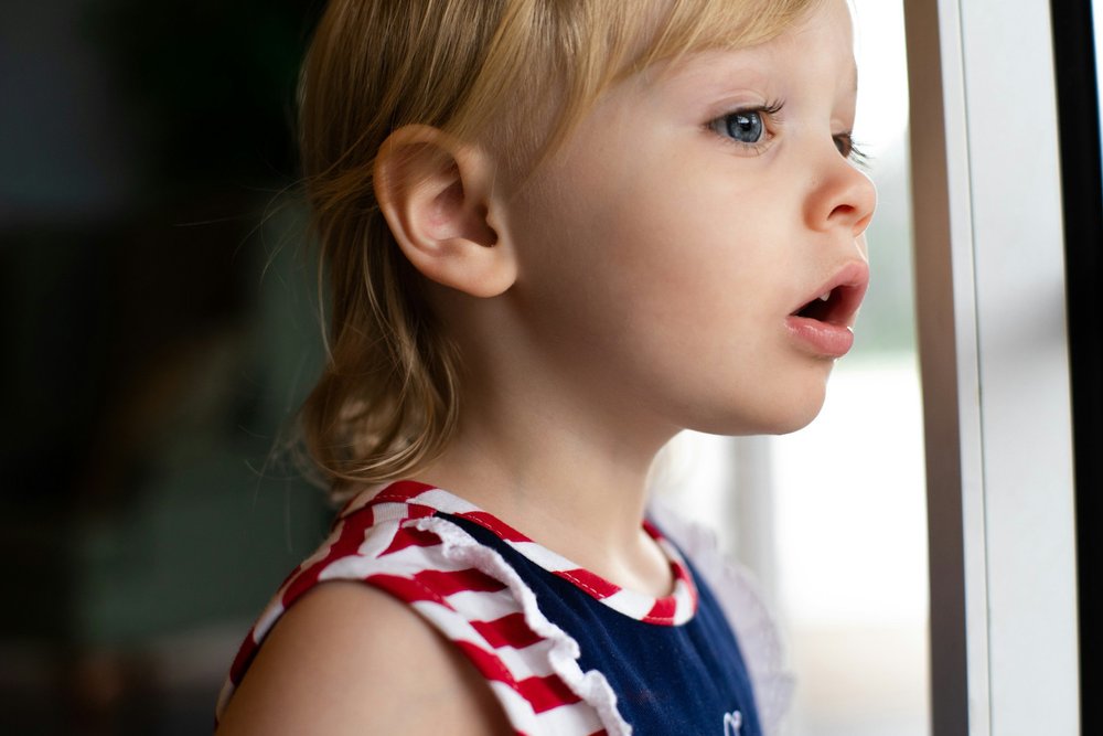 A child standing against a dark background with both hands over their face