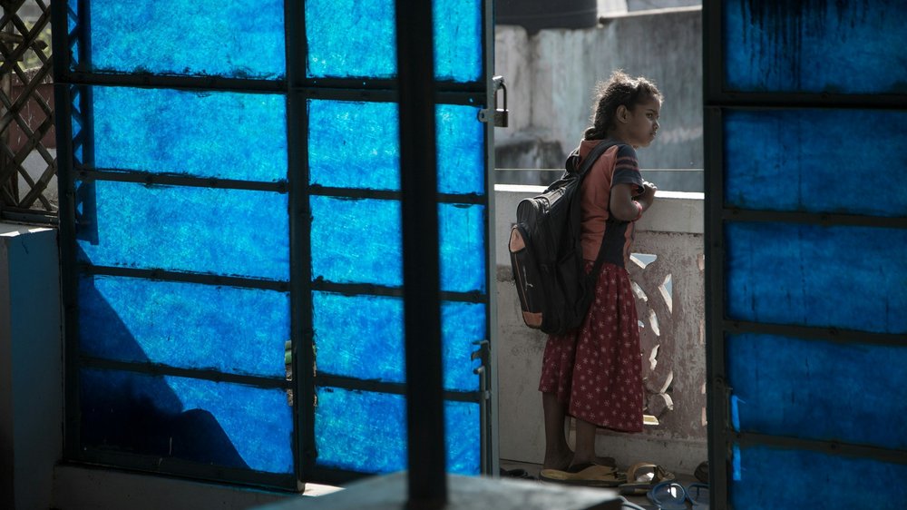 A child in a doorway lit blue, wearing a school backpack