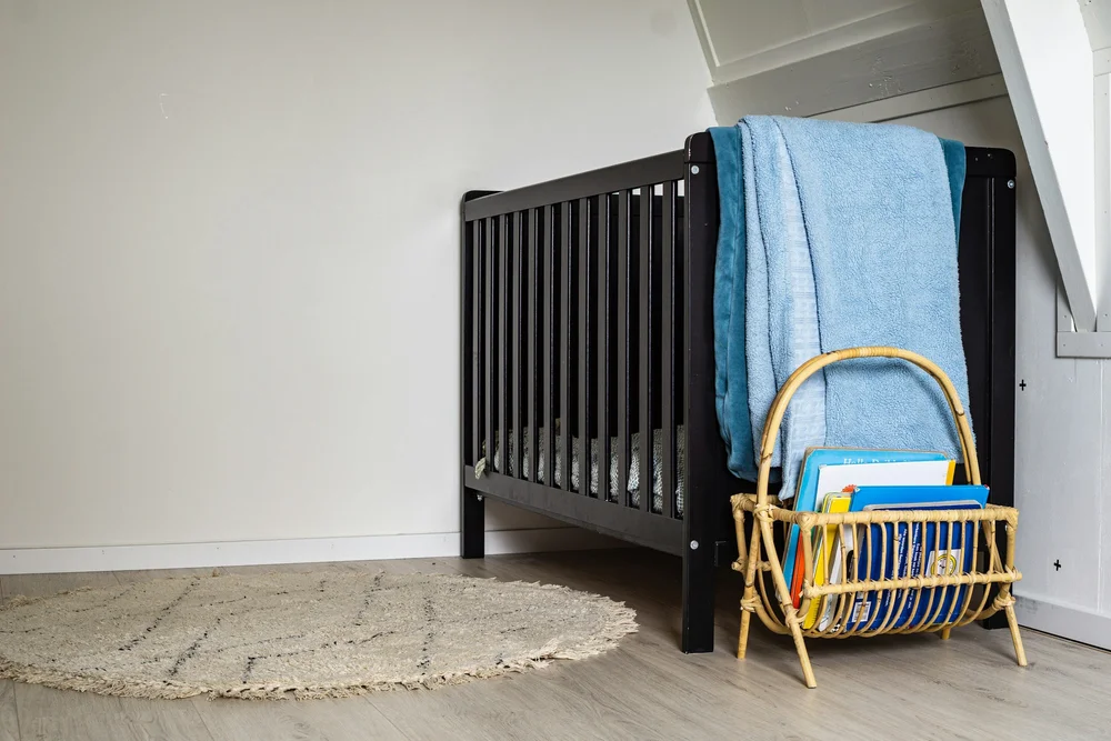 An empty nursery with a dark cot, a folded blanket and a small chair