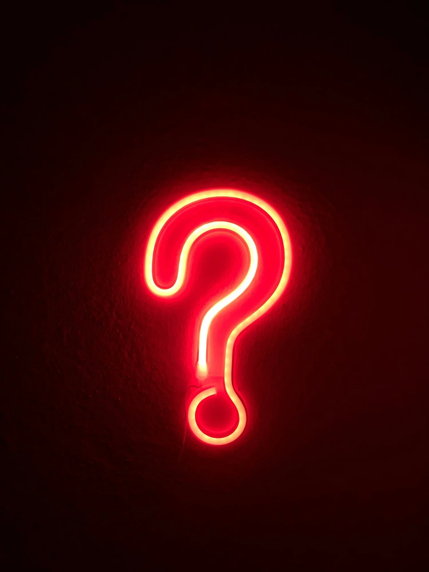 A red neon question mark on a dark wall