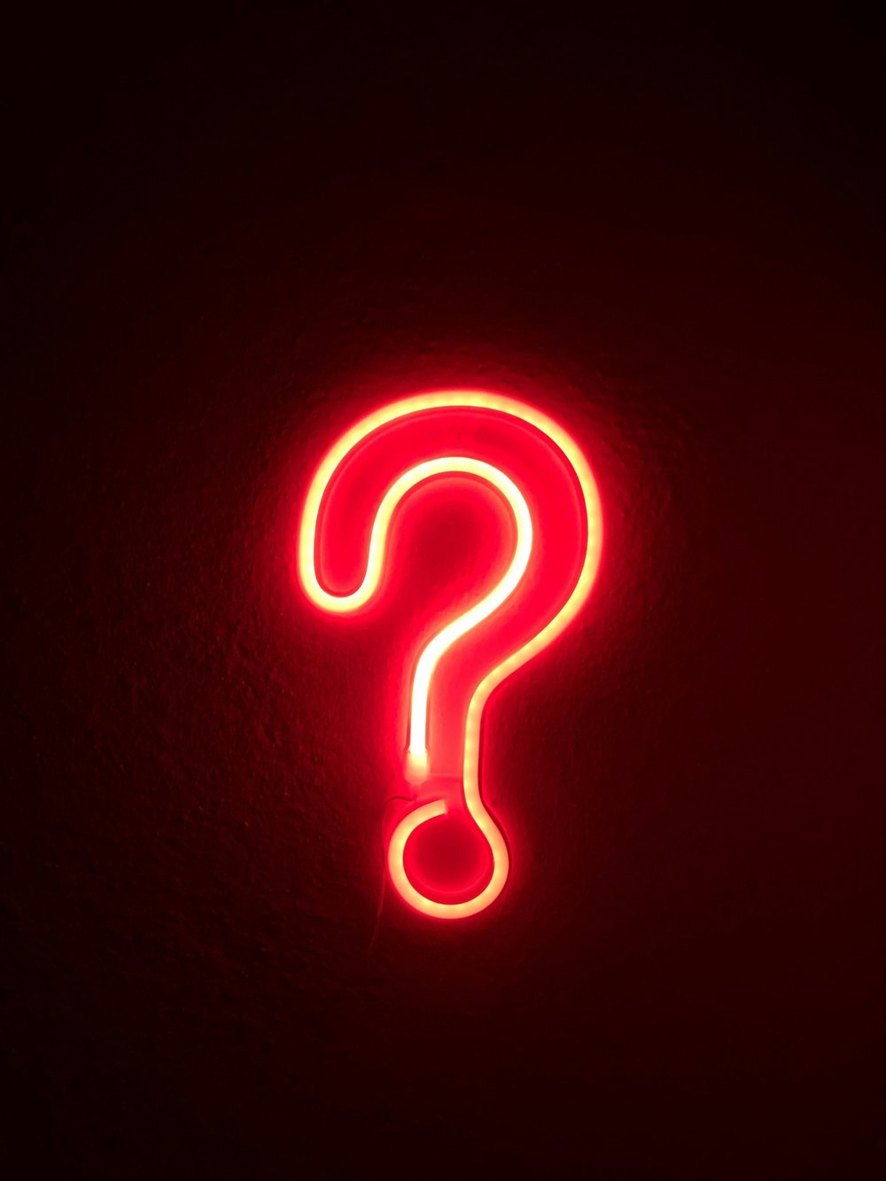 A red neon question mark on a dark wall
