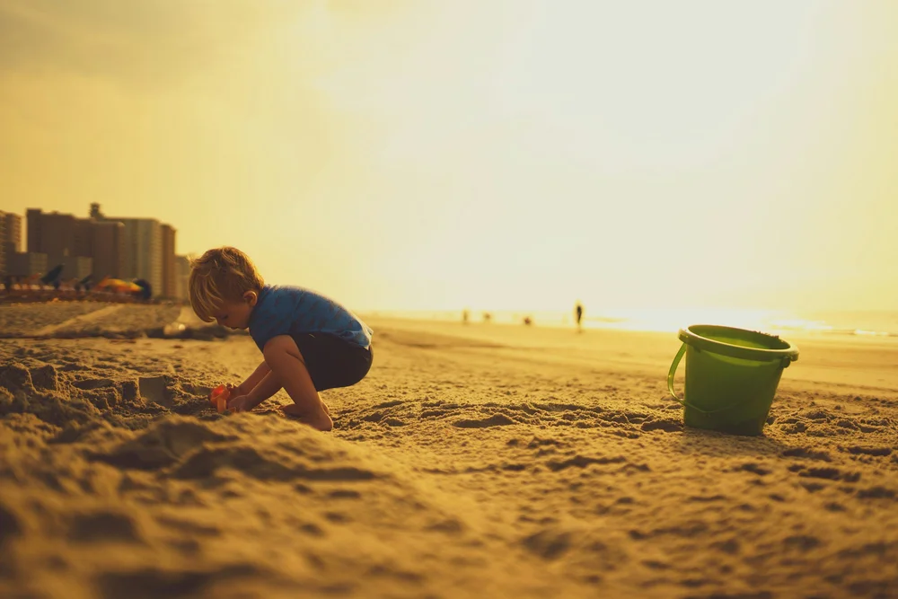 A child playing in the sand at the beach with a bucket