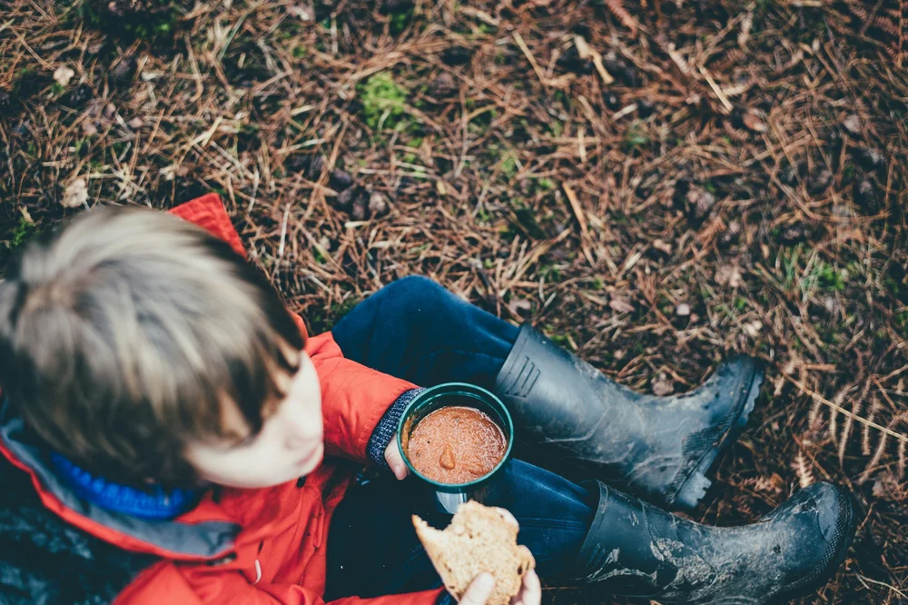 Overhead view of a child in a red coat and wellies sitting outside with a snack