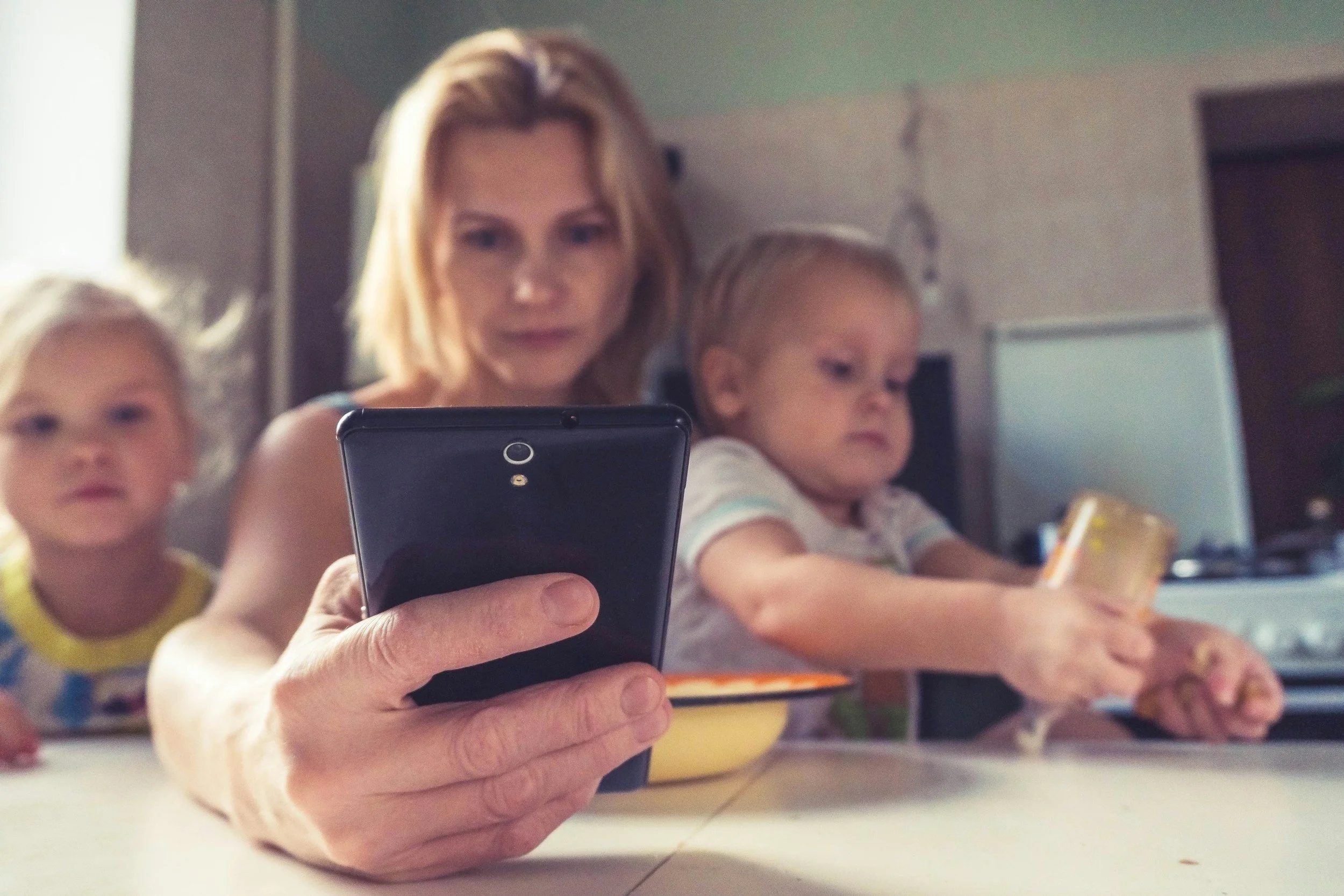 An adult and two young children looking at a tablet together at a kitchen table