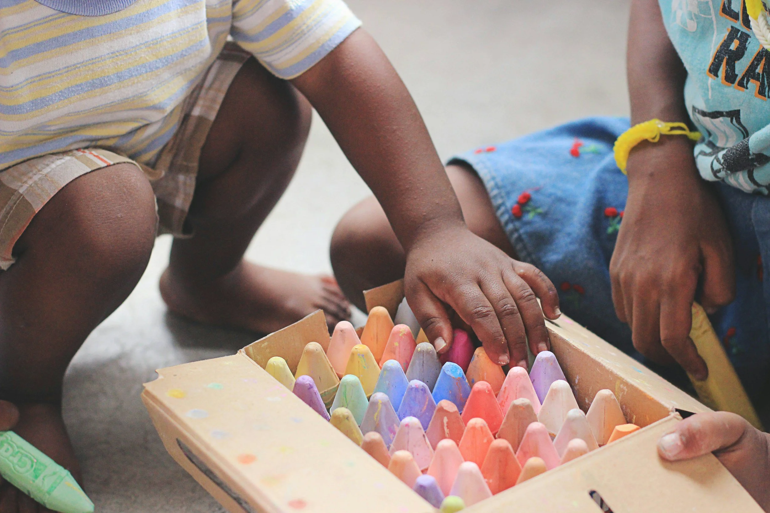 Children kneeling on the ground around a wooden box of coloured chalk