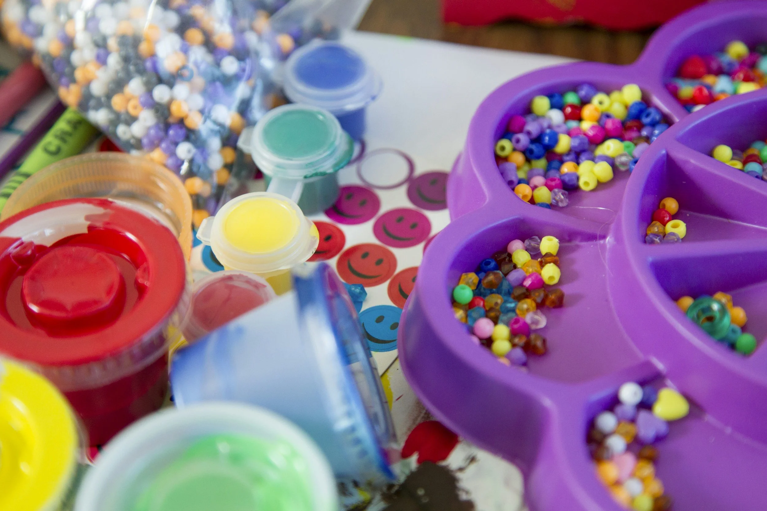 A tray of paint pots and coloured beads on a craft table