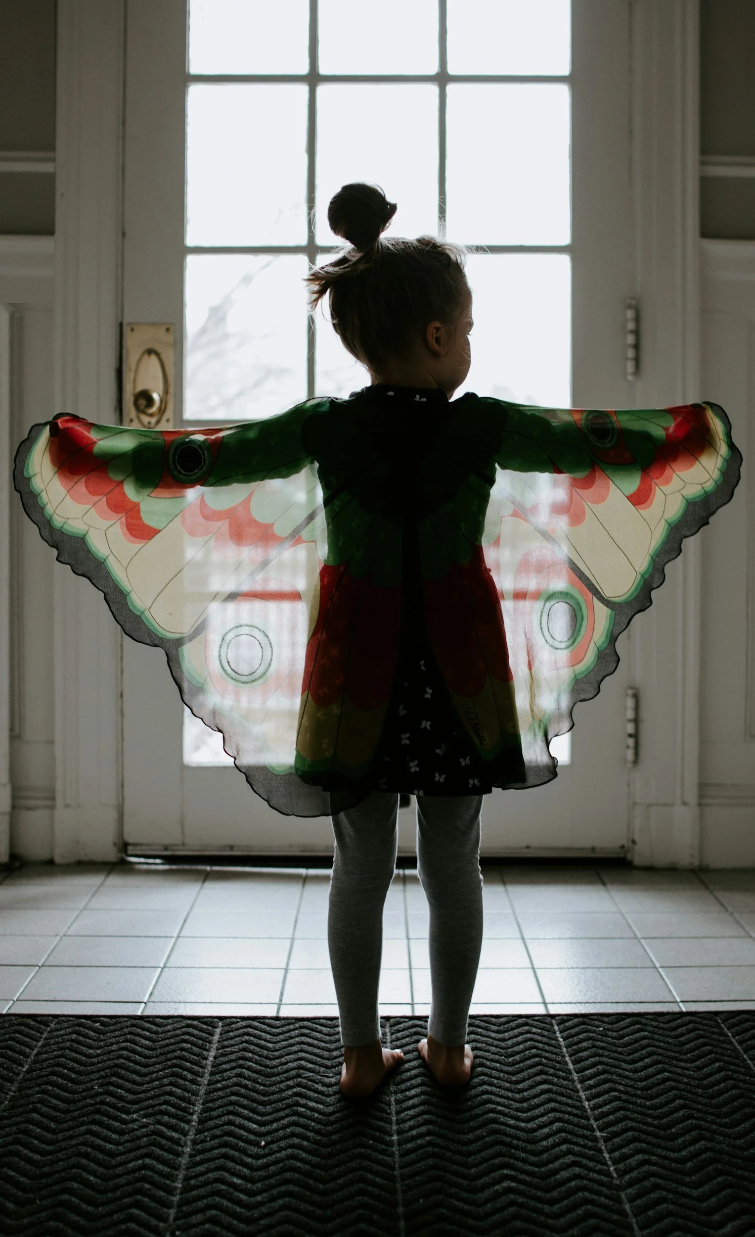 A child in a butterfly-wing costume standing in a doorway with arms outstretched