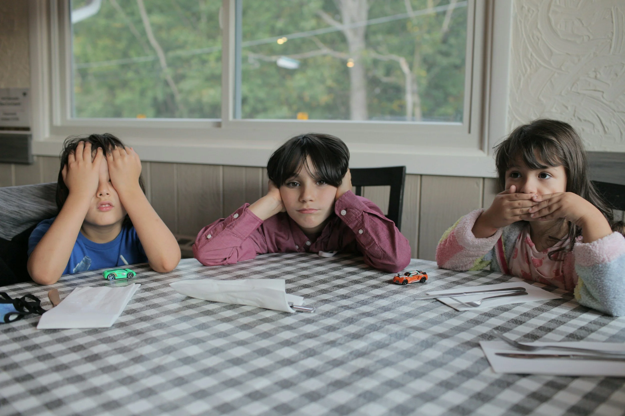 Three children sitting at a kitchen table looking restless and bored