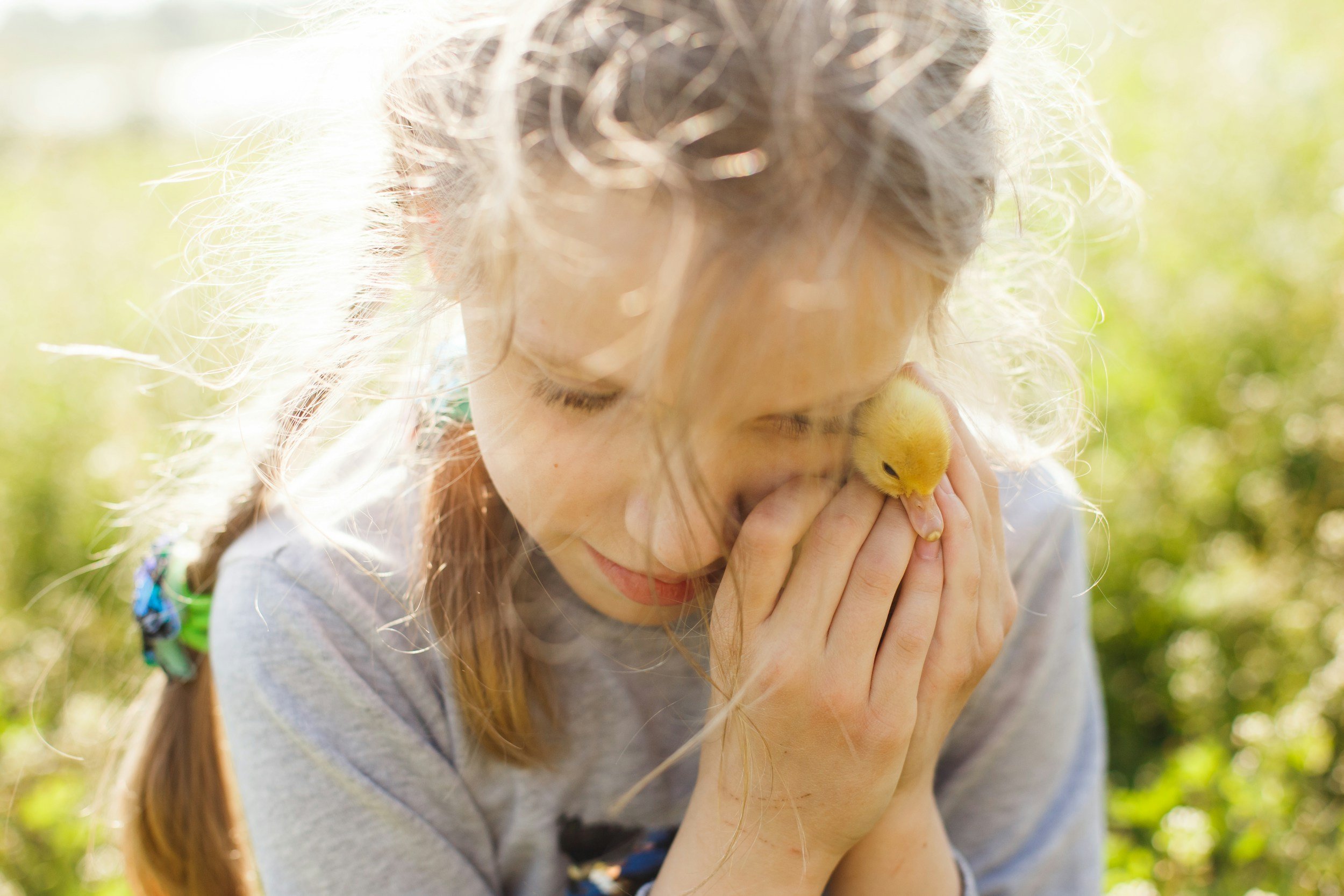 A girl outdoors holding a small yellow flower up to her face