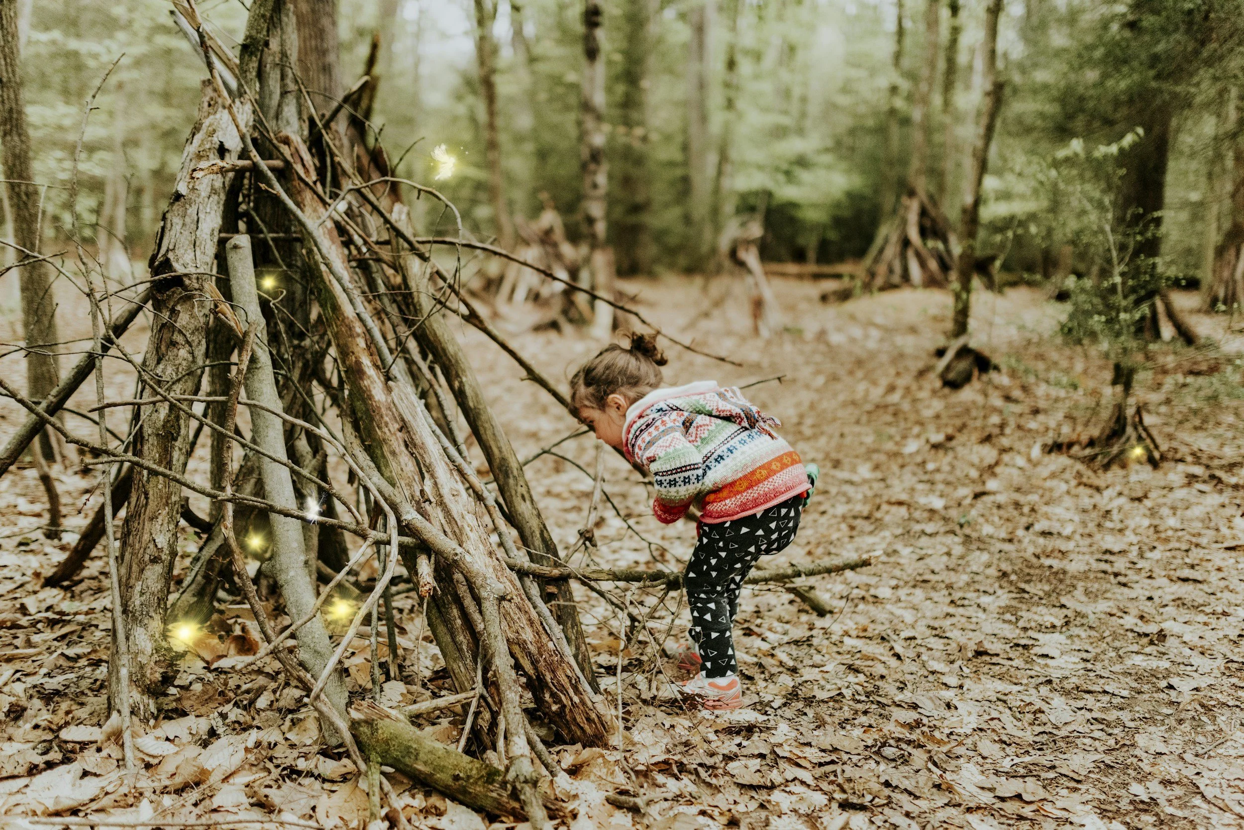 A child walking past a stick shelter in the woods