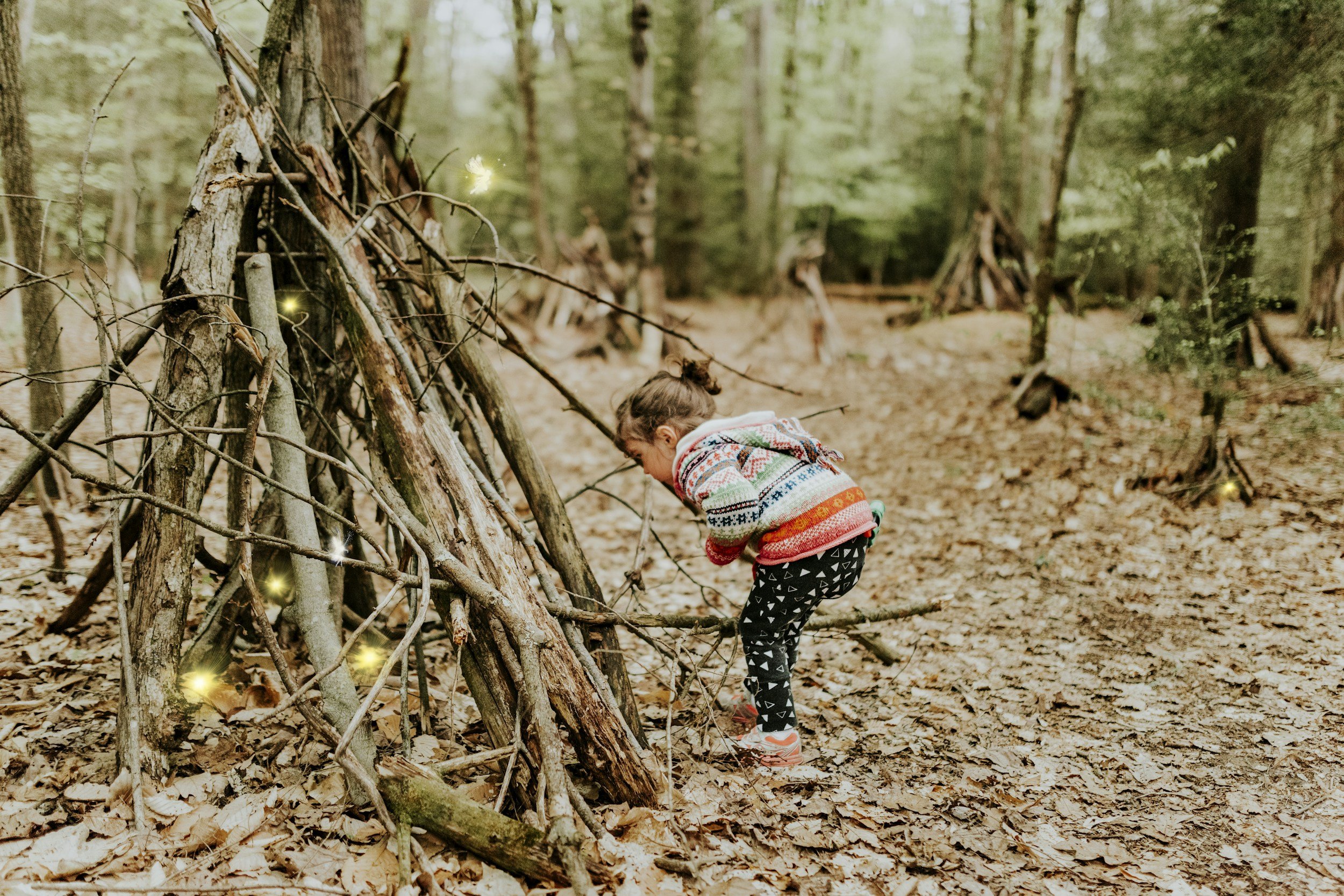 A child crouching beside a stick fort in the woods