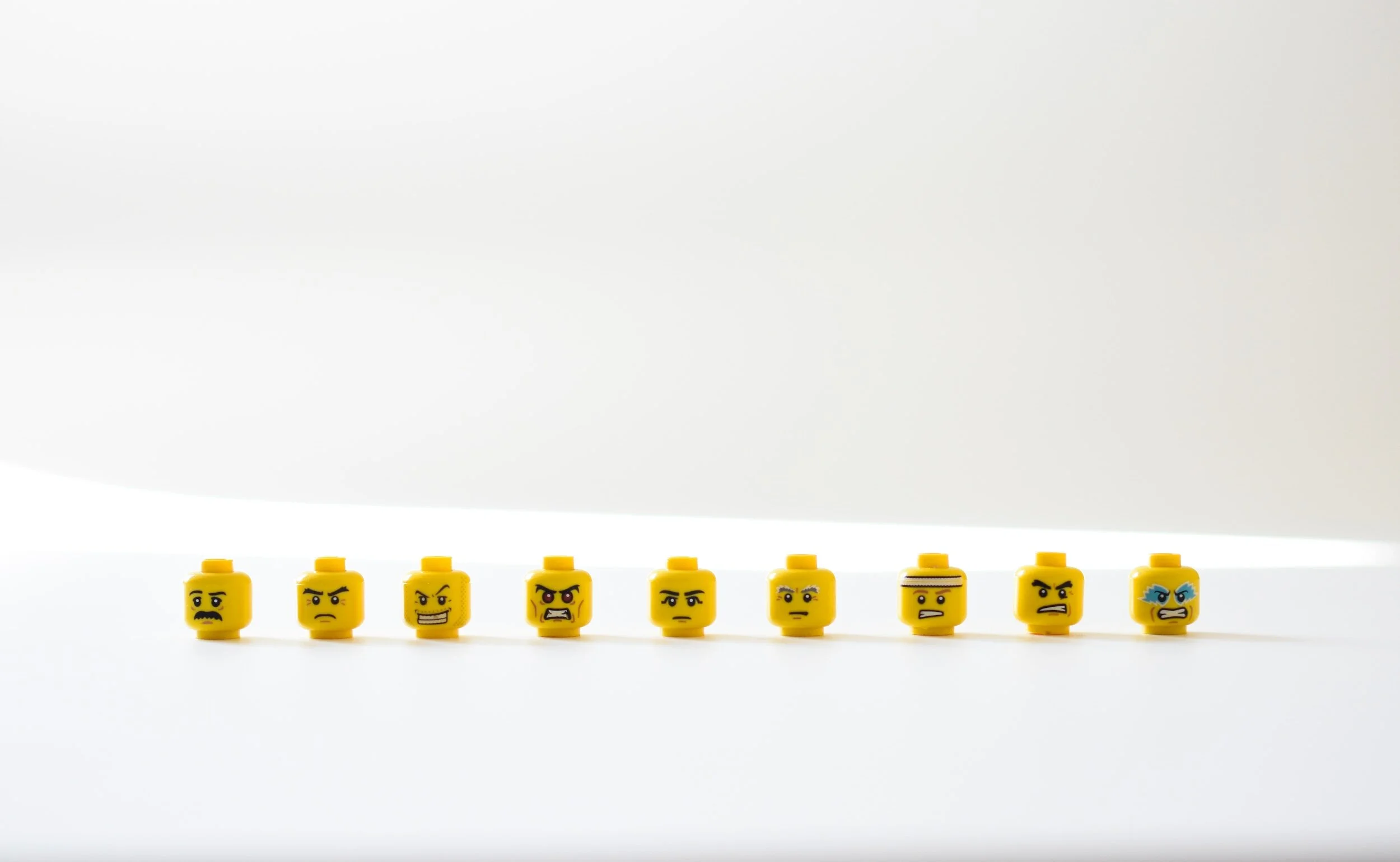 A row of small yellow toy figure heads with different facial expressions