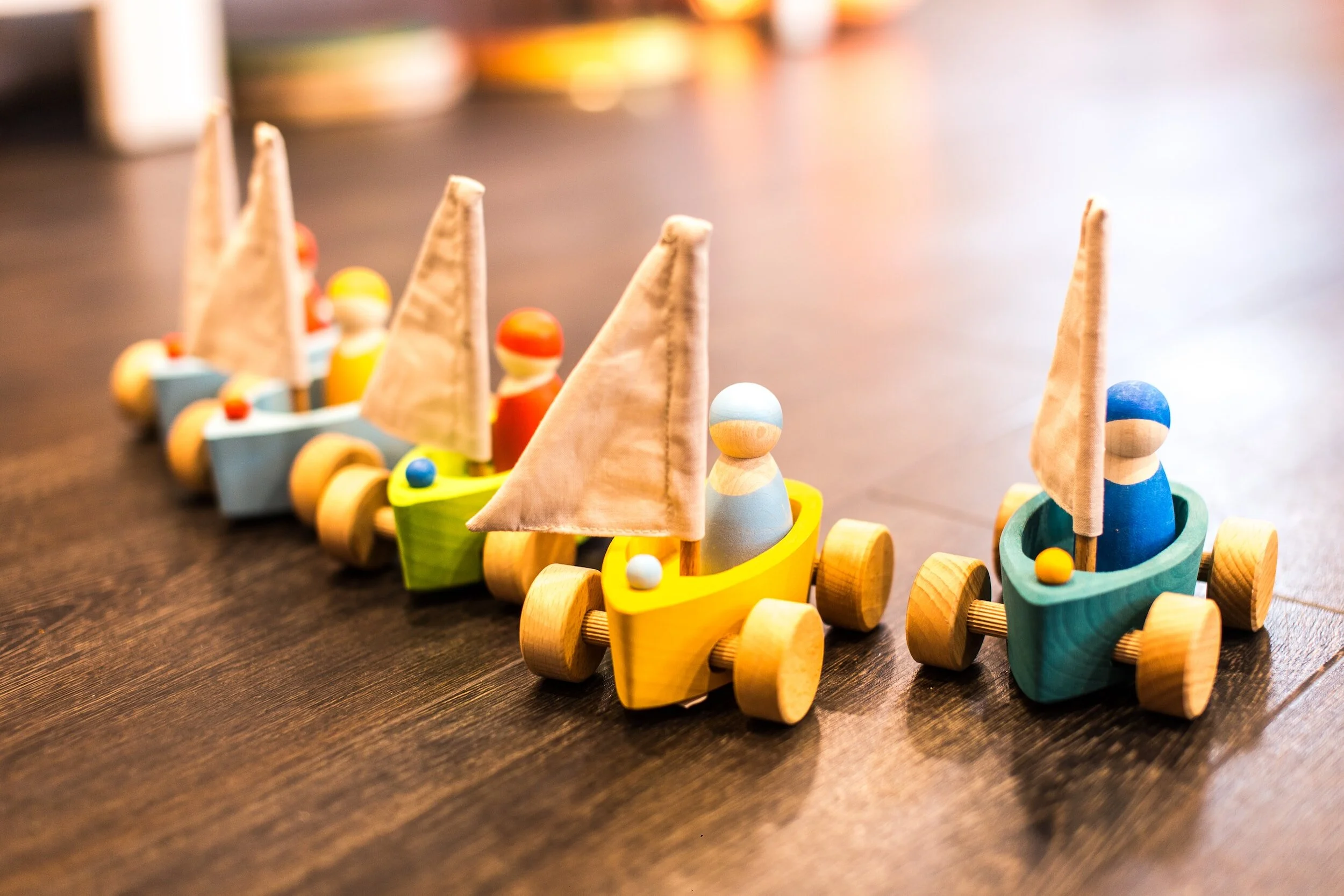 Small wooden toy cars with peg figures lined up on a table