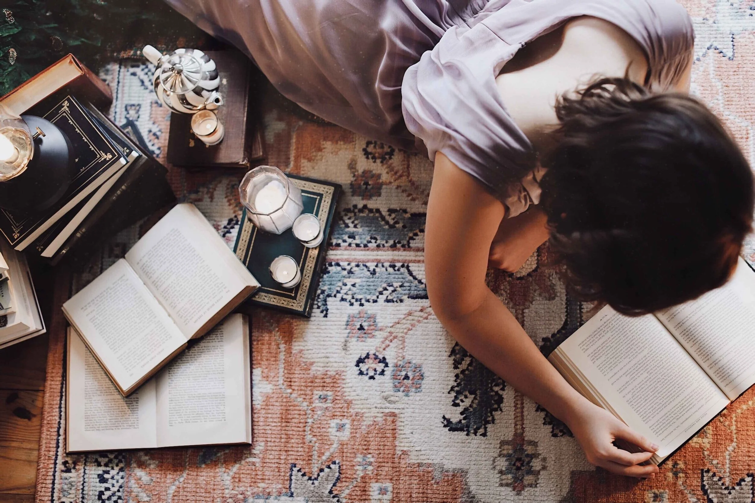 Overhead view of a child lying on a rug reading, books and objects around them