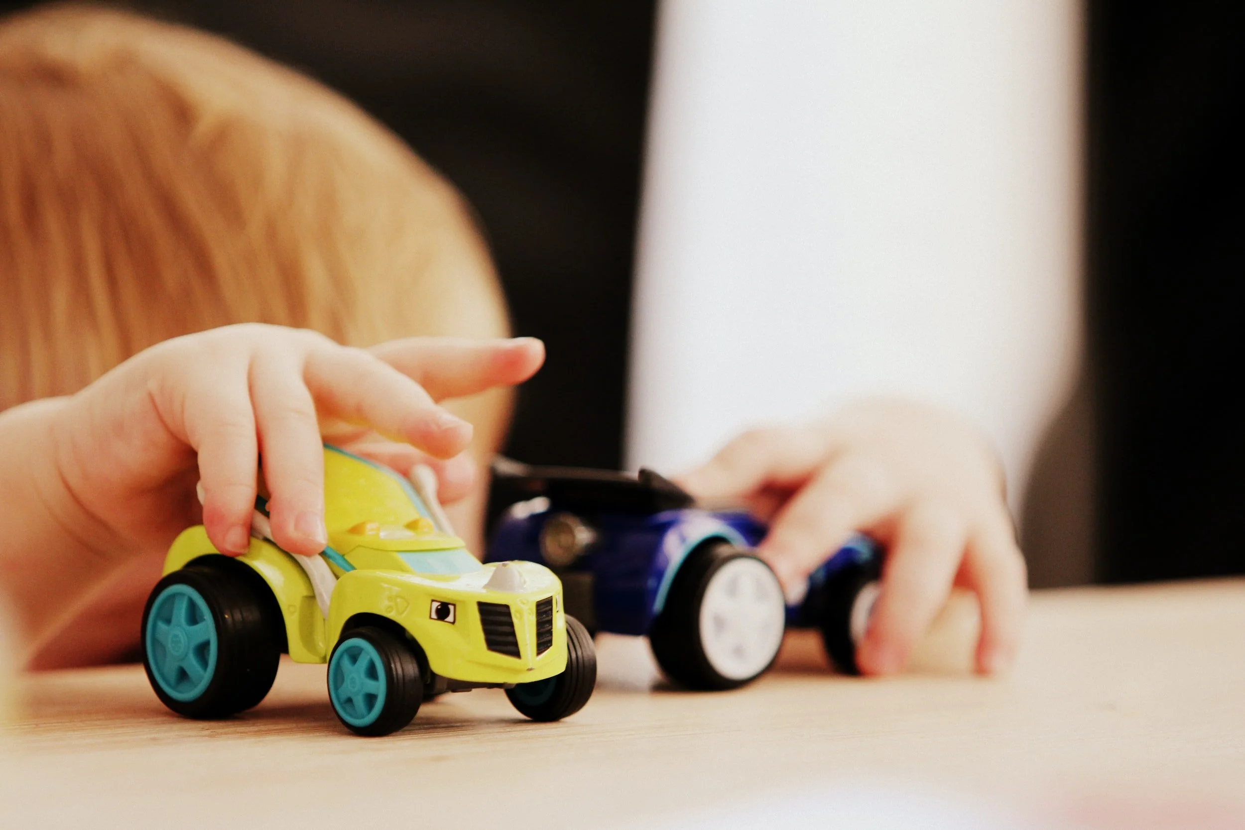 A child's hands pushing two toy cars together on a table