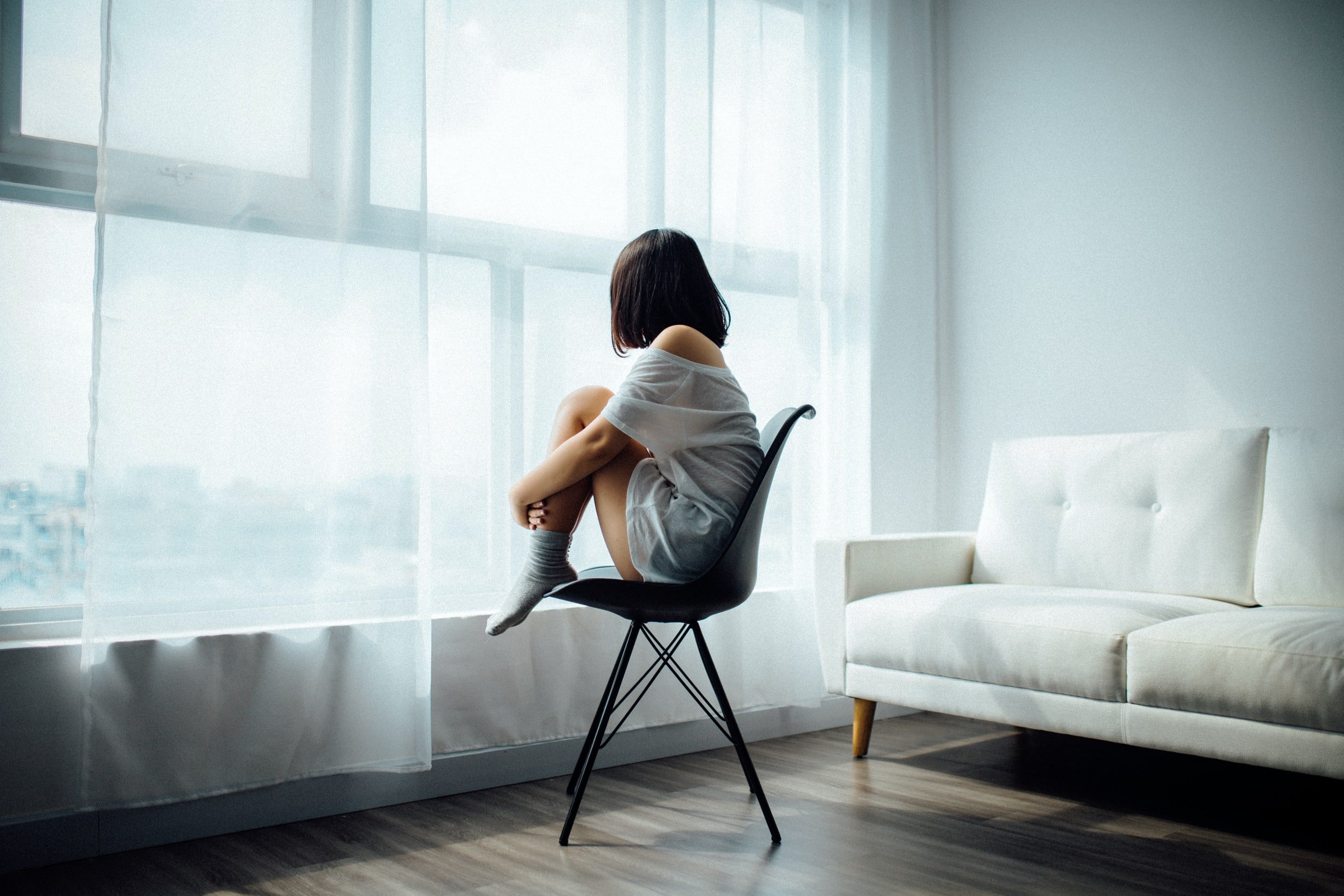 A child sitting on a chair by a bright window with their knees pulled up
