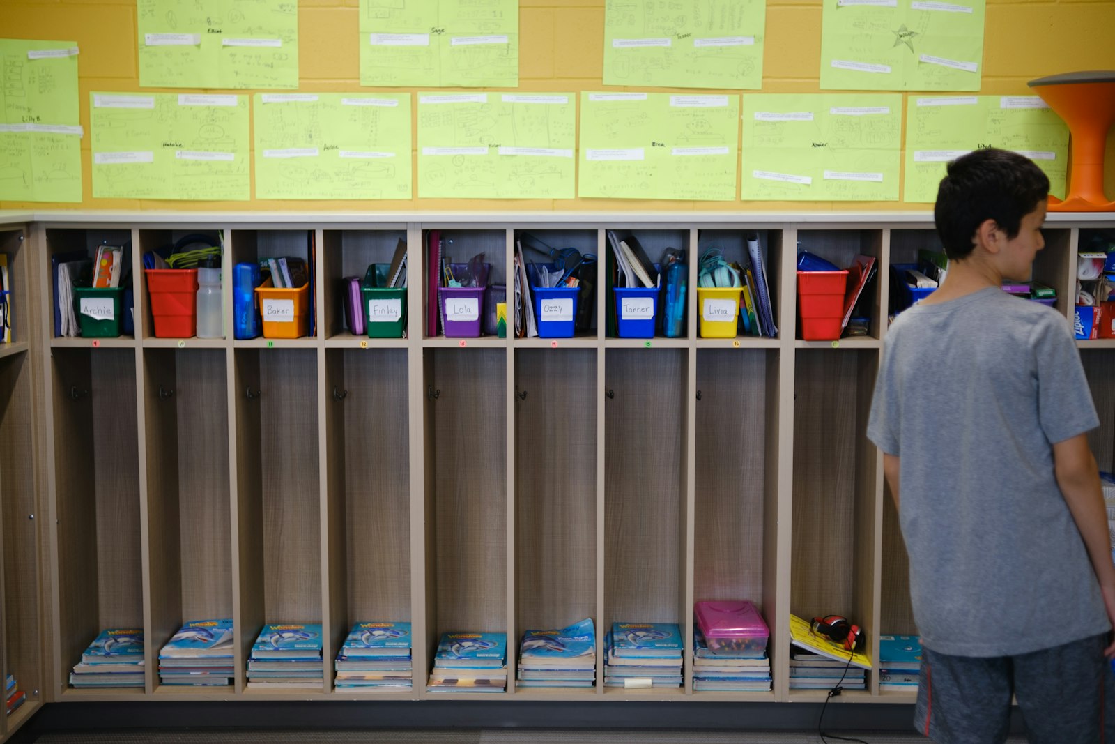 A child standing at classroom cubbies with named bins on the first weeks of school, back to school anxiety in kids