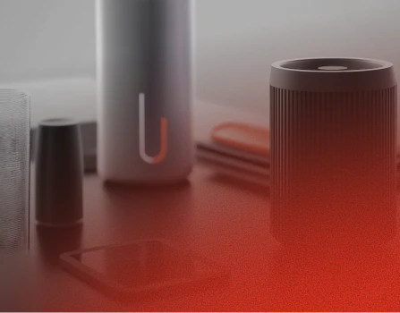 A close-up of modern electronic devices and accessories on a surface, including a cylindrical speaker with vertical grooves and a tall metallic bottle with a U-shaped symbol, all set in a softly lit environment with a reddish gradient overlay at the bottom right.