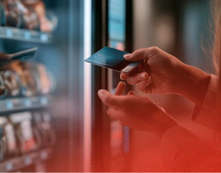 Person holding a credit card in front of a vending machine with blurred snacks inside.