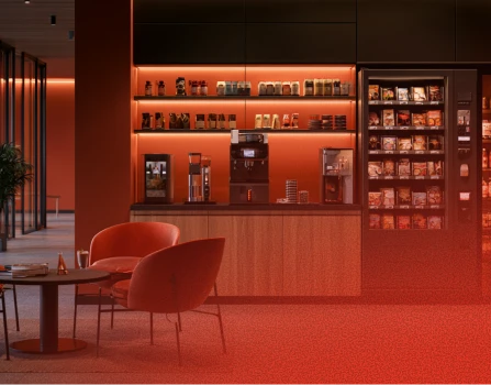 Modern coffee bar with illuminated shelves displaying coffee jars and equipment, a coffee machine on the counter, and a vending machine with snacks to the right, accompanied by a round table and orange cushioned chairs.