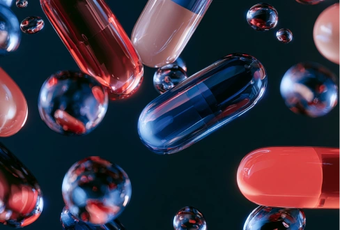 Close-up of red, pink, and blue capsules suspended among glossy bubbles against a dark background.