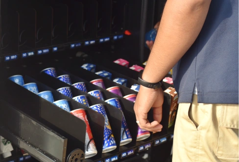 Person selecting a packaged snack from a vending machine stocked with colorful products.