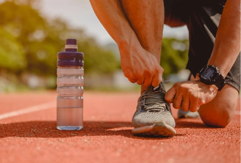 Runner tying a shoe on an outdoor track with a reusable water bottle beside them.