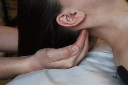 A hand cupped gently under a client's neck, below the ear, during manual lymphatic massage