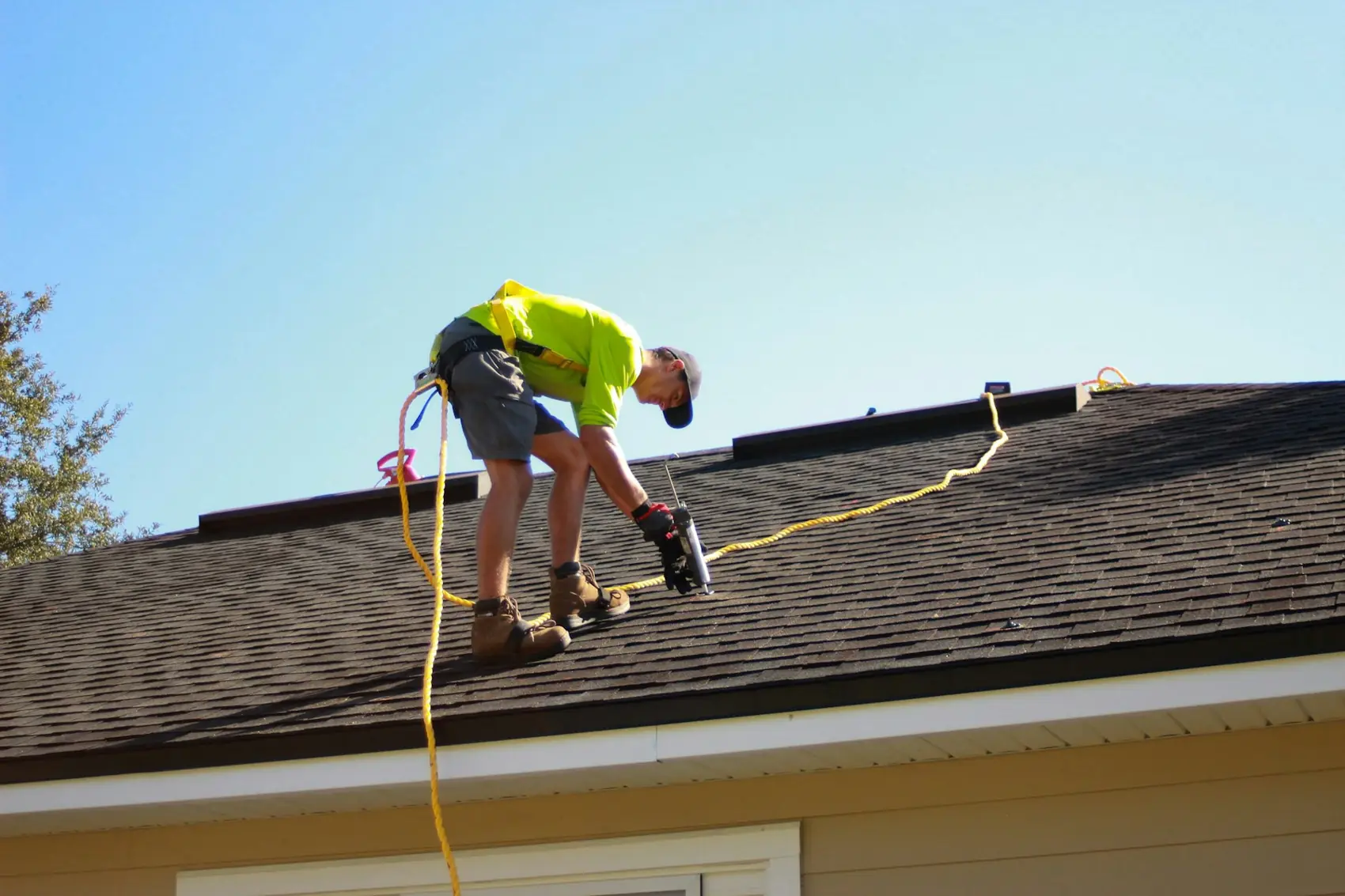 Roofer working on an asphalt shingle roof with a safety line