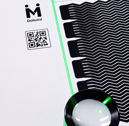 Acetate plate artwork with zigzag lines, magnifying glass, QR code, and Dolumi logo on white background.