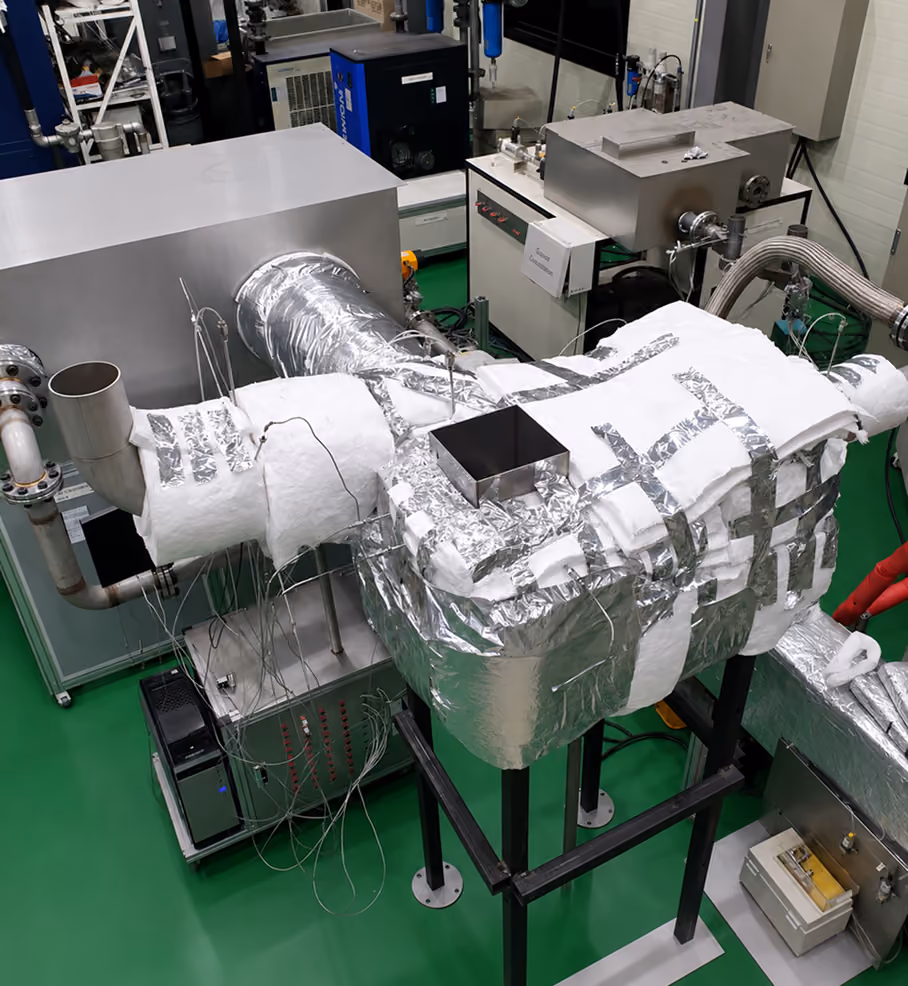 Insulated industrial machine system with metal ducting and attached sensors in a green-floored lab.
