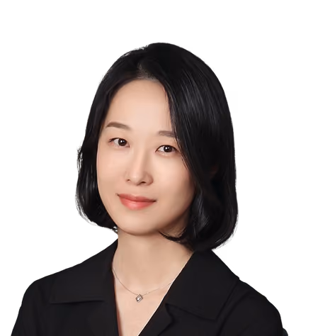 Portrait of a woman with straight black hair wearing a black top and a necklace, against a black background.
