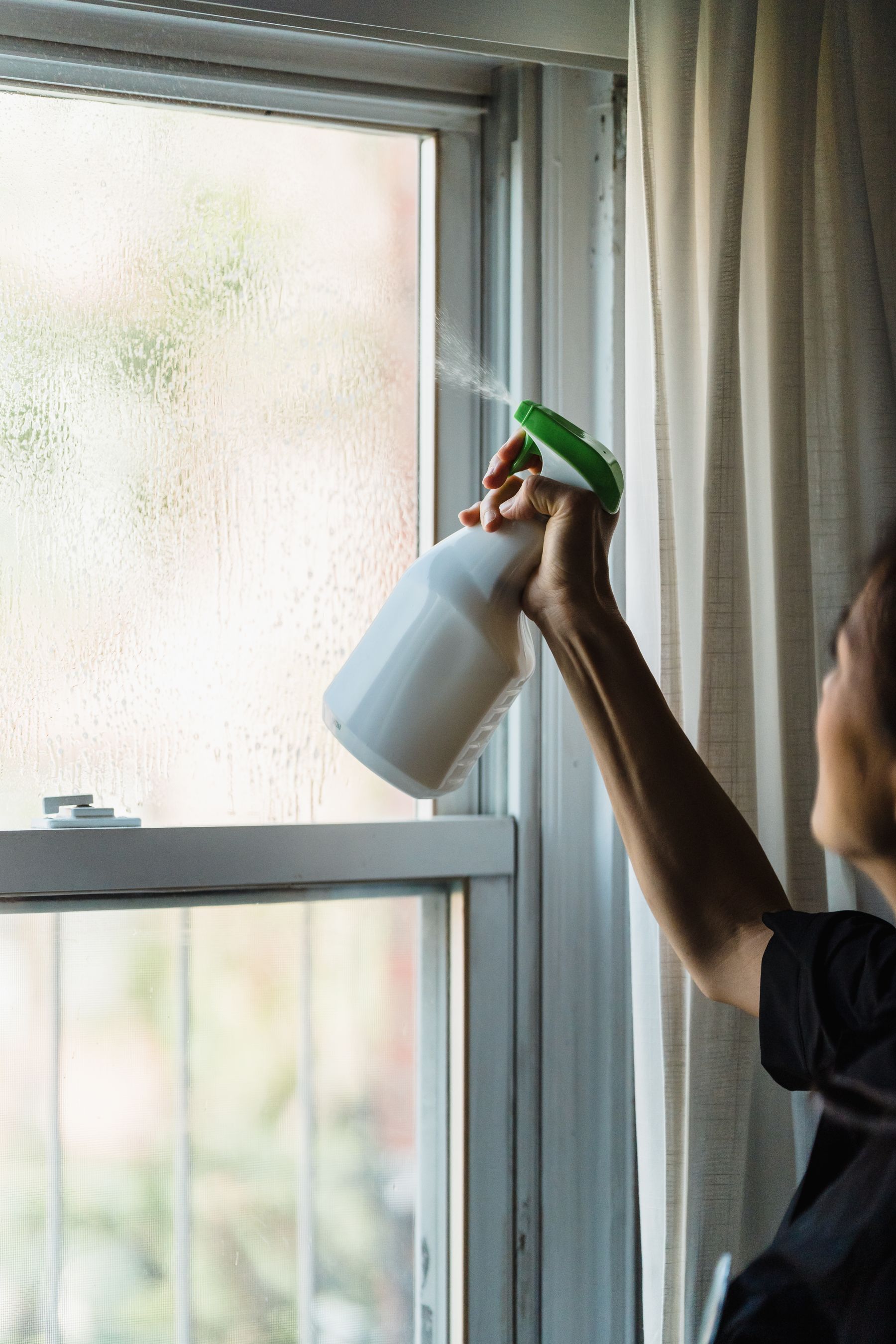 Person cleaning the glass and frame of a residential window as part of routine maintenance