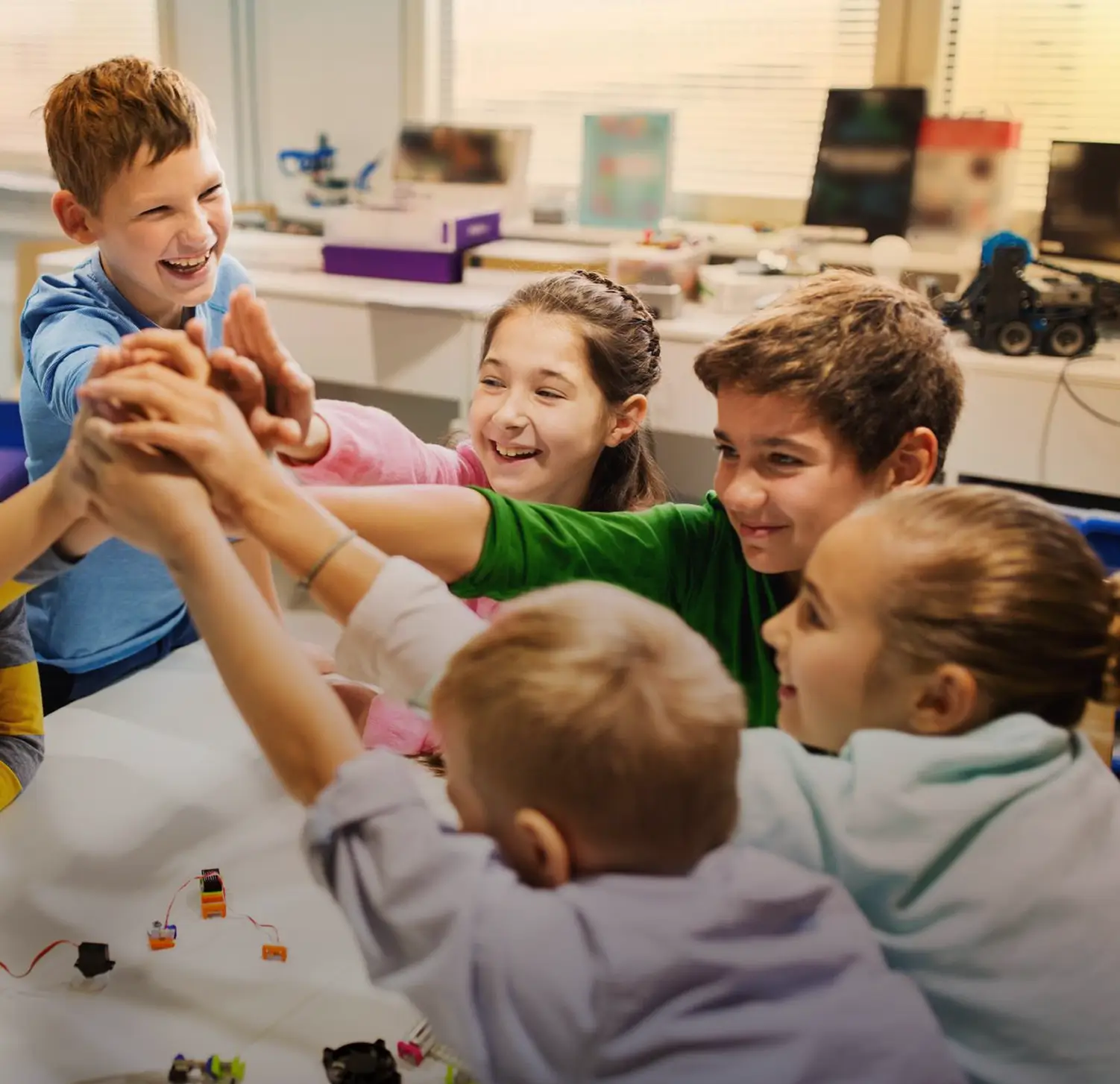 Group of five children sitting around a table smiling and joining hands in a high-five.