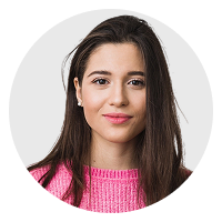 Portrait of a young woman with long dark hair wearing a pink sweater and small earrings.