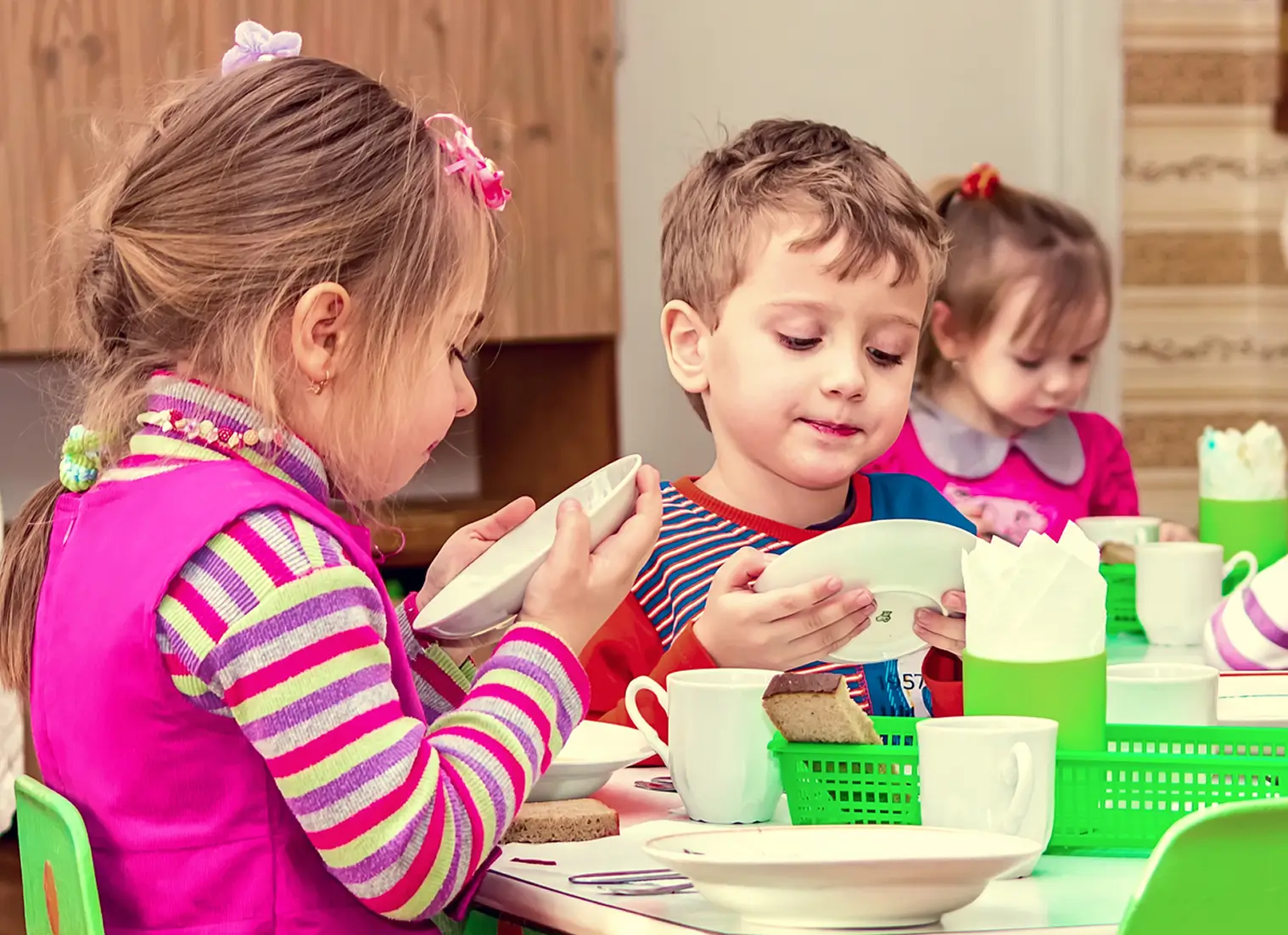 Two children planting seeds in a white planter filled with soil on a table with other pots and plants.