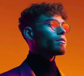 Side profile of a man with curly hair and round glasses against an orange background.