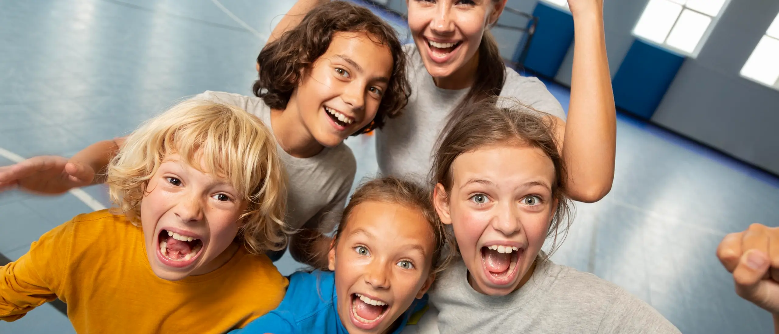 A group of four excited children and one adult in a gym celebrating with big smiles, some raising their fists in the air.