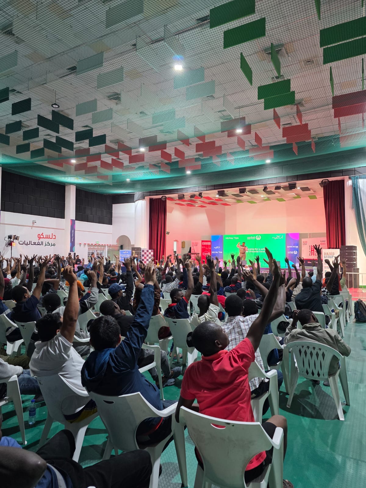 Large audience of workers raising their hands at a myZoi community event in a sports hall