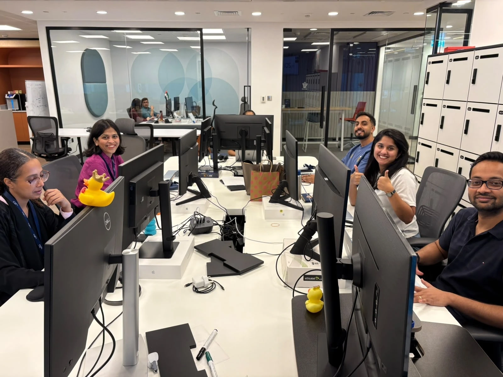 Smiling team members at their desks in an office with yellow rubber ducks on the monitors